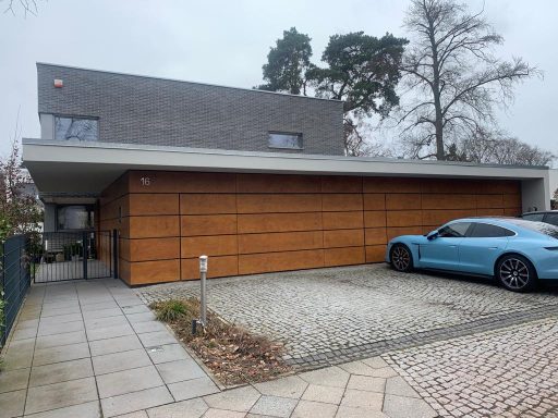 Modernes Haus mit Holzverkleidung, Garagenplatz und blauem Auto im Vordergrund.