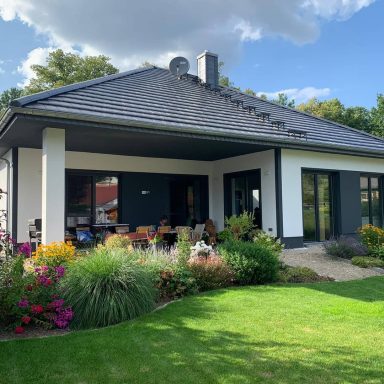 Moderne Villa mit großem Garten, Terrasse und bunten Blumenbeeten.